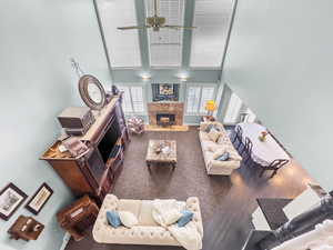 Living area with a towering ceiling, a premium fireplace, ceiling fan, and dark colored carpet