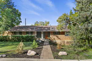 Ranch-style house with brick siding, a front yard, a chimney, and covered porch