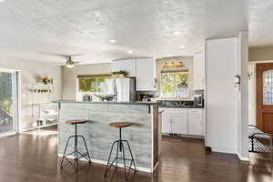 Kitchen featuring dark countertops, white cabinets, a kitchen island, kitchen bar, and LVP Flooring