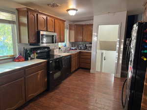 Kitchen featuring black appliances, dark wood-type flooring, light countertops, tasteful backsplash, and brown cabinets
