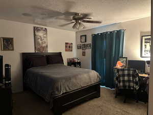 Carpeted bedroom featuring a textured ceiling, ceiling fan, and a desk