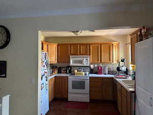 Kitchen featuring white appliances, light countertops, dark wood-type flooring, brown cabinets, and crown molding