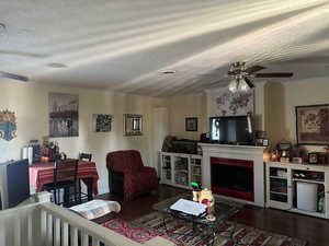 Living area featuring a ceiling fan, crown molding, dark wood-style floors, a textured ceiling, and a fireplace