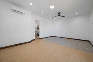 Unfurnished room featuring light wood-style flooring, arched walkways, stacked washer / dryer, a wall unit AC, and a ceiling fan