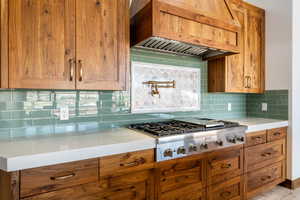 Kitchen featuring decorative backsplash, custom exhaust hood, light stone counters, and brown cabinets