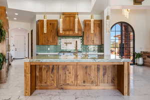 Kitchen featuring light marble finish floors, brown cabinetry, arched walkways, backsplash, and recessed lighting
