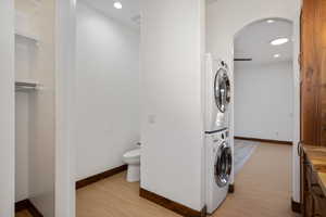 Washroom with arched walkways, stacked washing machine and dryer, recessed lighting, and light wood-type flooring