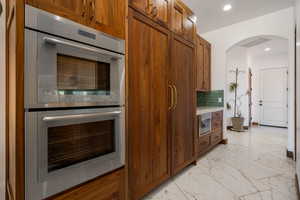Kitchen with double oven, light marble finish flooring, brown cabinets, tasteful backsplash, and light countertops