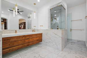 Bathroom featuring a marble finish shower, double vanity, light marble finish flooring, a walk in closet, and recessed lighting