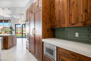 Kitchen with brown cabinetry, light marble finish floors, hanging light fixtures, tasteful backsplash, and built in appliances