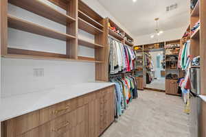 Spacious closet featuring light colored carpet and a chandelier