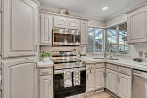 Kitchen featuring stainless steel appliances, light countertops, crown molding, white cabinets, and recessed lighting