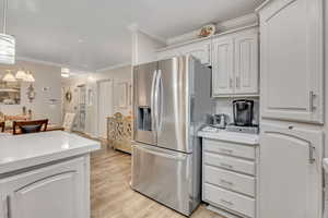 Kitchen with stainless steel fridge with ice dispenser, light wood finished floors, white cabinets, ornamental molding, and decorative light fixtures