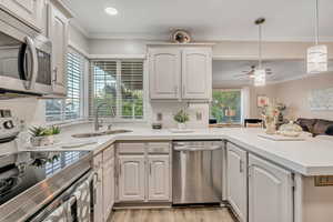 Kitchen with stainless steel appliances, crown molding, decorative light fixtures, white cabinets, and light stone countertops