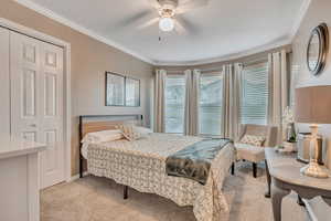 Bedroom featuring light colored carpet, ornamental molding, ceiling fan, and a closet