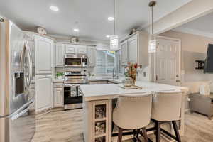 Kitchen featuring stainless steel appliances, a kitchen bar, decorative light fixtures, a peninsula, and crown molding
