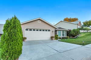 Ranch-style home featuring concrete driveway, a front lawn, and a garage