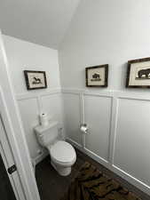 Bathroom with a decorative wall, dark wood-style floors, lofted ceiling, and wainscoting
