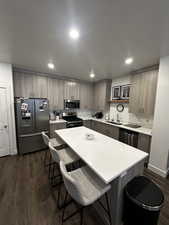 Kitchen with modern cabinets, stainless steel appliances, a breakfast bar, dark wood-style floors, and a kitchen island