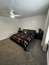 Bedroom with dark carpet, a textured ceiling, ceiling fan, and a decorative wall