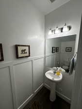 Half bathroom with a decorative wall, dark wood-style flooring, and a wainscoted wall