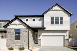 View of front facade with stone siding, driveway, an attached garage, and a gate