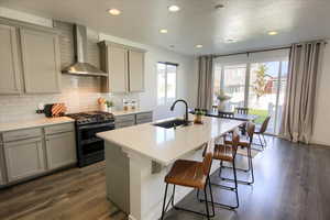 Kitchen with gray cabinets, wall chimney range hood, range with two ovens, backsplash, and recessed lighting
