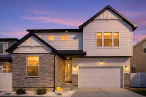 View of front of property with a gate, driveway, an attached garage, stone siding, and board and batten siding