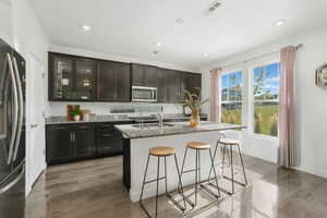 Kitchen featuring light stone counters, refrigerator with ice dispenser, a kitchen breakfast bar, glass insert cabinets, and an island with sink
