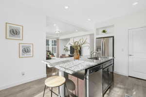 Kitchen featuring appliances with stainless steel finishes, an island with sink, recessed lighting, light wood finished floors, and a breakfast bar area