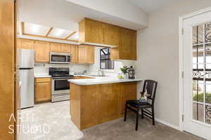 Kitchen with a peninsula, light countertops, appliances with stainless steel finishes, a breakfast bar, and light carpet