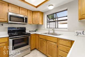 Kitchen with stainless steel appliances, light countertops, light tile patterned floors, and brown cabinets