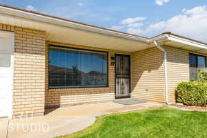 Doorway to property featuring brick siding, a yard, and a porch
