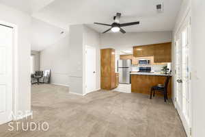 Kitchen with lofted ceiling, brown cabinetry, light colored carpet, a peninsula, and stainless steel appliances
