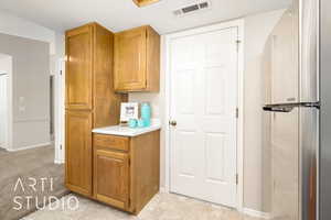 Kitchen with freestanding refrigerator, light countertops, brown cabinets, and light carpet