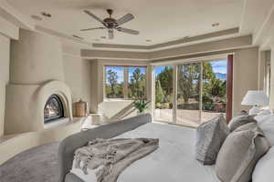Bedroom featuring a glass covered fireplace, access to outside, multiple windows, a tray ceiling, and recessed lighting