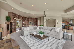 Living room with recessed lighting, light stone finish flooring, arched walkways, and built in features