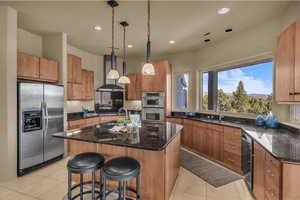 Kitchen with stainless steel appliances, dark stone counters, hanging light fixtures, a kitchen island with sink, and a breakfast bar area