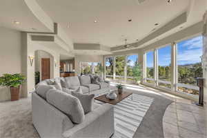 Living area with a tray ceiling, ceiling fan, recessed lighting, arched walkways, and light colored carpet