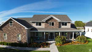 Craftsman-style house featuring stone siding, covered porch, roof with shingles, and a front yard