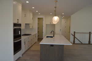 Kitchen featuring a kitchen island with sink, light stone counters, hanging light fixtures, white cabinets, and appliances with stainless steel finishes
