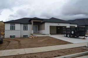 View of front of property with concrete driveway, a shingled roof, an attached garage, and stone siding
