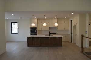 Kitchen featuring a kitchen island with sink, hanging light fixtures, white cabinetry, recessed lighting, and light wood-style floors
