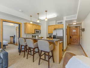 Kitchen with a peninsula, light brown cabinets, a breakfast bar, dark stone counters, and hanging light fixtures