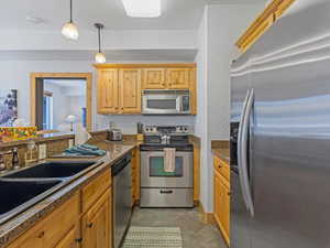 Kitchen with appliances with stainless steel finishes, pendant lighting, dark tile patterned flooring, dark stone counters, and a textured wall