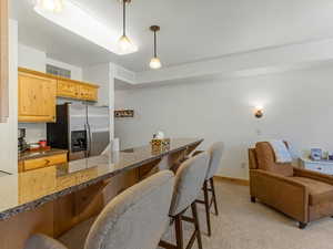 Kitchen featuring a kitchen breakfast bar, stainless steel refrigerator with ice dispenser, light brown cabinets, and dark stone countertops