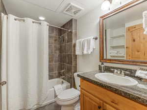 Bathroom with a textured wall, shower / tub combo with curtain, vanity, and dark tile patterned floors