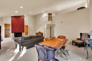Carpeted dining space featuring a towering ceiling, recessed lighting, a large fireplace, and stairs