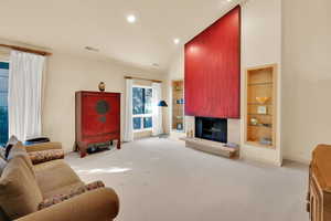 Carpeted living area with built in features, a fireplace with raised hearth, high vaulted ceiling, and recessed lighting