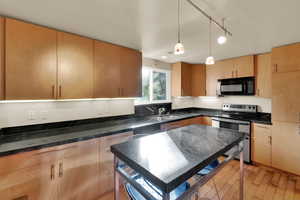 Kitchen with stainless steel electric range oven, hanging light fixtures, black microwave, light wood-style flooring, and light brown cabinets